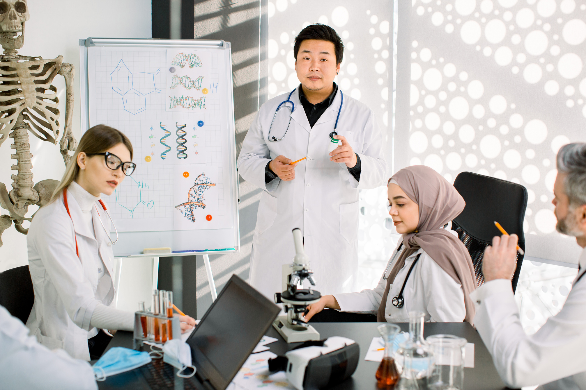 Biochemistry, pharmacology, drug industry, clinical trials. Young Asian doctor talks about the results of clinical trial of new medicine, having a meeting with his multiracial coworkers scientists